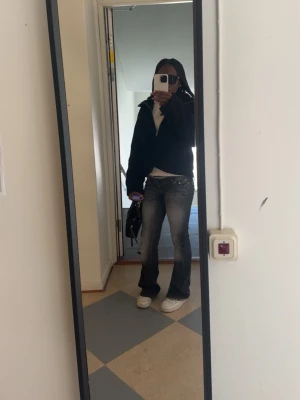 Bootcut jeans i tvättad blå denim - Säljer ett par bootcut jeans i tvättad grå denim med snygga slitningar och ljusare partier på låren. Jeansen har låg midja och klassisk femficksmodell. Perfekta för dig som gillar en retro och avslappnad stil.