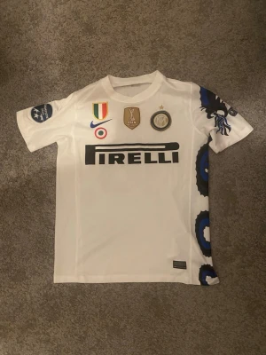 Inter Milan Sneijder matchtröja - Vit Inter Milan matchtröja med Sneijder 10 på ryggen. Tröjan har blå och svarta detaljer längs sidan, Pirelli-logga på bröstet och flera klubbmärken och patchar. Tillverkad i lätt och ventilerande material, perfekt för fotboll eller samling.