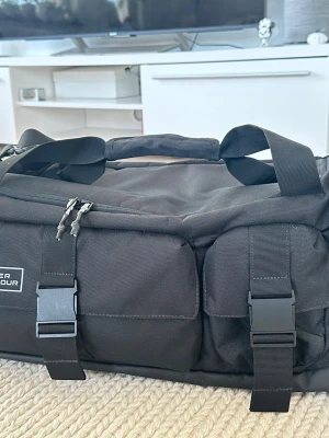 Under Armour Svart Gametime Pro Duffelväska - Svart duffelväska från Under Armour. Väskan har ett stort huvudfack, flera sidofickor och en ficka för skor. Den har både handtag och en justerbar axelrem för bekväm transport. Väskan är utrustad med UA Storm-teknologi som ger en vattenavvisande yta. 42L  Mått:38,1 x 29 x 55,1 cm