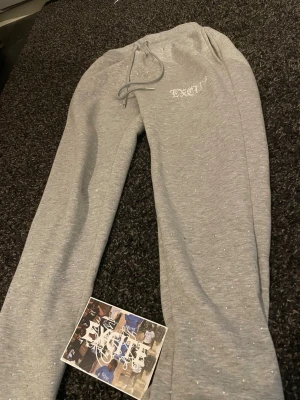 Grå mjukisbyxor från Exet - Snygga grå mjukisbyxor från Exet med dragsko i midjan och diskreta små stenar över hela byxan för extra stil. Byxorna har en relaxed fit och är perfekta för chill dagar. Tillverkade i mjukt material som känns skönt mot huden.