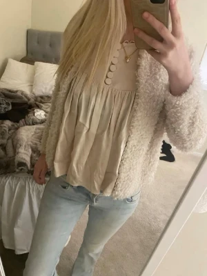 Krämvit fluffig cardiganjacka - Mysig och fluffig cardiganjacka i krämvit färg. Jackan har en kortare modell och är tillverkad i ett mjukt, teddyliknande material. Få 10% rabatt om du både köper cardigan och blusen🤍🤩