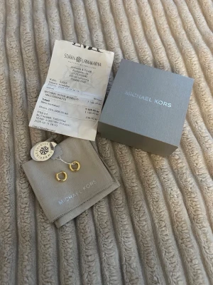Örhängen Michael Kors - Michael kors örhängen aldrig använda helt nya. Örhängena har en klassisk rund form och kommer med originalpåse och ask. 