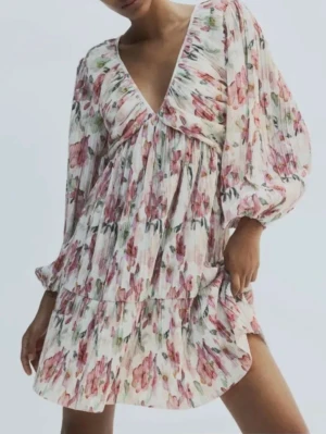 Blommig kortklänning med volang HM - Supersöt kortklänning med blommigt mönster i rosa, grönt och vitt. Klänningen har v-ringning, långa ärmar och volangdetaljer. Tillverkad i ett lätt, plisserat material som ger en luftig känsla. Perfekt för vår och sommar! Bortklippt lapp men skulle tro Max s/m ( enligt mig )