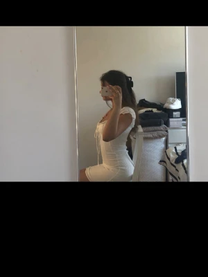 Vit kort klänning -  Vit kort klänning med puffärmar. Klänningen har en liten knytning vid urringningen och är figurnära med en lätt volangkant. Perfekt för sommarens, midsommar eller studenten 