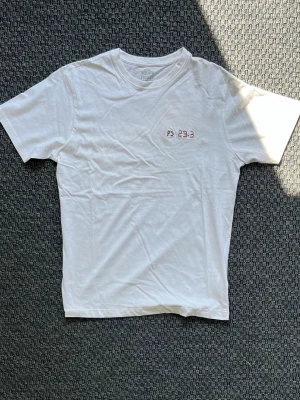 Handbroderad vit T-shirt från Denim Project - Vit T-shirt med handbroderad text ”PS 23:3”. "Han ger mig ny kraft och leder mig på rätta vägar, sitt namn till ära."