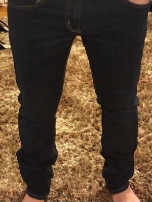 Mörkblå slim fit jeans - Säljer ett par mörkblå slim fit jeans med klassiska fem fickor och kontrastsömmar. Jeansen har en smal passform och är tillverkade i ett stretchigt denimtyg som sitter snyggt på benen. Perfekta för dig som gillar en stilren och enkel look. C52