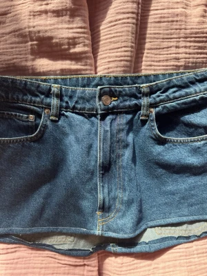 Mörkblå jeanskjol med fickor - Säljer en snygg mörkblå jeanskjol i klassisk denim med fem fickor och gul kontrastsöm. Kjolen har bälteshällor och knappstängning framtill. Perfekt för dig som gillar en enkel men trendig stil. sytt om själv 💞