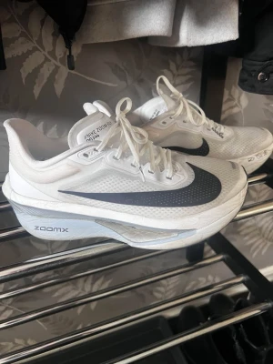 Nike ZoomX Vita Sneakers - Nike ZoomX sneakers i vitt med stor svart swoosh på sidan. Skorna har en sportig design med mesh-överdel för bra ventilation och tjock, dämpad sula med ZoomX-teknologi. Perfekta för dig som gillar stilrena och tekniska sneakers.