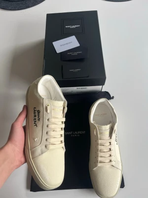 Saint Laurent vita låga sneakers - Snygga vita sneakers från Saint Laurent med klassisk låg siluett. Skorna är tillverkade i canvas med vita snören och har Saint Laurent-loggan tryckt på sidan och tungan. Perfekta för dig som gillar stilrena och exklusiva detaljer. Skickas samma dag dem köps, skriv gärna vid frågor😊