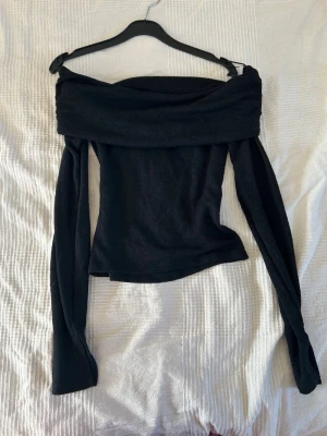 Svart offshoulder topp - Trendig svart offshoulder topp med långa ärmar och bred krage som vilar över axlarna. Toppens material känns mjukt och stretchigt, perfekt för en stilren look. Passformen är figurnära och toppen är enkel att matcha med olika outfits. Bara använd 1 gång💗