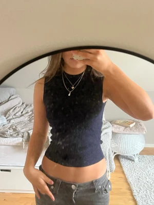 Mörkblå ribbad ärmlös topp - Säljer en mörkblå, ribbad och croppad ärmlös topp med hög hals. Toppen har en tight passform och är tillverkad i ett stretchigt material som sitter snyggt på kroppen. Perfekt att styla med jeans eller kjol.