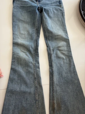 Blå bootcut jeans med slitningar - Säljer ett par klassiska blå bootcut jeans med snygga slitningar och tvättade detaljer. Jeansen har normalhög midja, fem fickor och utsvängda ben. Perfekta för en avslappnad och trendig look.