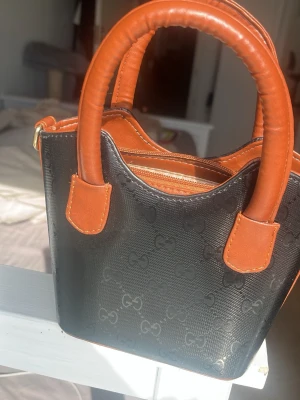 Svart och brun handväska  - En snygg liten handväska perfekt för dig som inte orkar bära på stora väskor! Den är gammal men aldrig använd inga skador eller något.