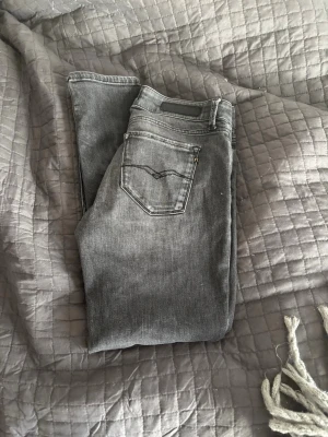 Grå slim fit jeans från Replay - Snygga grå slim fit jeans från Replay med klassisk femficksdesign och diskreta slitningar. Jeansen har dragkedjegylf och svarta detaljer vid fickorna. Perfekta för en trendig och avslappnad look.