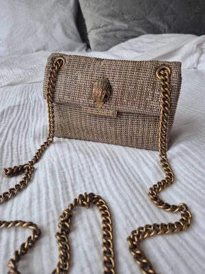 Guldig Kurt geiger väska  - Väskan är använd en del men fortfarande i mycket bra skick. En liten slitning finns på undersidan av väskan(se bild) men märks ej när man använder den. Samt att kedjan tappat lite färg men märks inte heller. Nypris 2200kr