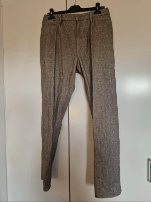 Grå Byxor från Dondup w31 - Snygga grå kostymbyxor med rak passform och pressveck. Byxorna har bälteshällor, framfickor och en bakficka med knapp. Materialet ser ut att vara en ullmix med diskret struktur, perfekta för en clean och stilren look.