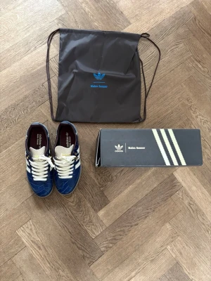 Adidas x Wales Bonner blå sneakers - Unika Adidas x Wales Bonner sneakers i blått med vit sula och klassiska tre ränder på sidan. Ovandelen har croc-mönstrad finish och detaljer i vitt, samt grova vita snören och gulddetaljer vid snörningen. Kommer med originalpåse och låda.