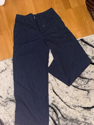 Mörkblå randiga kostymbyxor  - Säljer ett par mörkblå kostymbyxor från SHEIN i storlek XS. Byxorna har smala vita ränder, raka ben och klassisk midja. Perfekta för en stilren look och lätta att matcha med olika toppar. Materialet känns lätt och bekvämt.