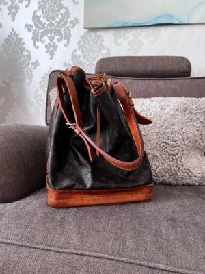 Loui Vuitton NOE shoulder bag - Säljer nu min äkta Louis Vuitton NOE shoulder bag. Väskan är i fint skick men med visst slitage. Slitaget går att se på sista bilden. Väskan är rymlig och man får plats med en bärbar dator i den. Där finns äkthetsintyg på väskan och det kommer skickas med vid försäljning. Inköpt i Köpenhamn på Collectors Cage sommaren 2024. 