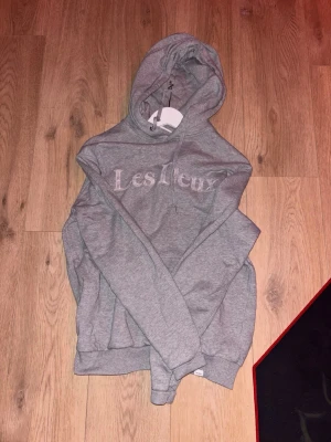 Grå hoodie från Les Deux - Snygg grå hoodie från Les Deux med broderad logga på bröstet. Klassisk modell med huva och dragsko samt ribbade muddar vid ärmslut och nederkant. Tillverkad i mjukt bomullsmaterial för skön känsla. Perfekt för en avslappnad och stilren look. Nu är den förliten på mig så tänker att jag vill ha en bra slant för denna. Den är skön som fan. Haft på mig den 5 gånger typ och sen ser den bra ut. Storlek S men skulle säga att den är till 145-160. Vill att den ska få en bra ägare!  Går att sänka pris! 