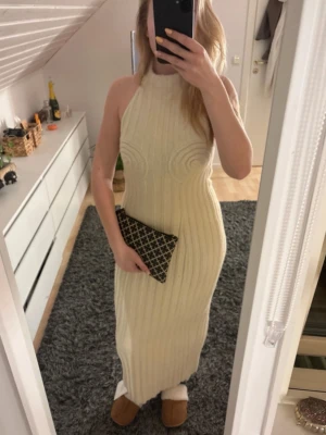 Lång ribbad klänning från Adoore - Snygg långklänning från Adoore i ljus beige färg. Klänningen är ribbstickad med hög hals och är ärmlös, vilket ger en stilren och modern look. Perfekt för dig som gillar minimalistisk stil och vill ha något bekvämt men ändå trendigt. Är i storlek L men passar mig som vanligtvis är storlek M. Klänningen är helt oanvänd och har lappen kvar! Orginalpris 1500. 