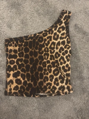 Leopardmönstrad one shoulder topp - Snygg leopardmönstrad topp med one shoulder-design. Toppen är ärmlös och har en tight passform, perfekt för att sticka ut. Materialet känns mjukt och följsamt mot huden.