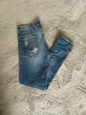 Replay jeans med snygga slitningar - Snygga blå  jeans med slitningar och tvättade detaljer. Klassisk femficksmodell med bra passform och normal midja. Jeansen har ljusare partier på låren och bakfickor med dekorativa sömmar. Perfekta för en avslappnad och trendig look. W28 L 32