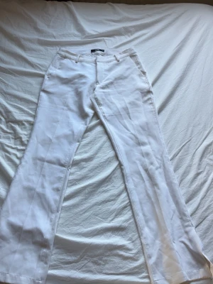 lågmidja vita kostymbyxor  - Stilrena vita kostymbyxor med vida ben och klassisk passform. Byxorna har hällor för skärp, fickor fram och bak samt stängs med dragkedja och knapp. Perfekta för en clean och dressad look. Materialet ser ut att vara en linneblandning.