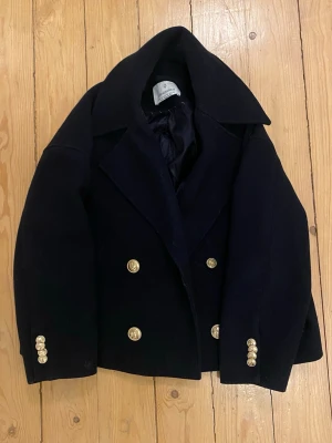 Marinblå skepparkavaj med guldknappar - Snygg mörkblå kappa med guldiga knappar. En av knapparna gick av och försvann, därför ersatte jag den med en liknande. Även om den inte är exakt samma tycker jag inte att det är något man tänker på. Jackan är i storlek XS men passar även S. 