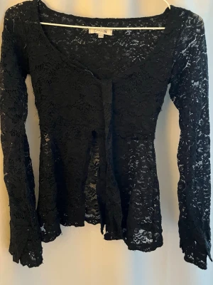 Svart spetskofta från Parisian - Säljer min fina långärmade topp från Design by Si. Toppen är i svart spets, v-formad urringning, med ett tillhörande spetsband där fram. Perfekt till alla tillfällen. Storlek XS/S