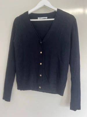 Mörkblå cardigan med guldiga knappar från Zara - Säljer denna mörkblåa cardigan från Zara i storlek S med v-ringning och guldfärgade knappar framtill. 