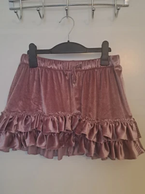 Rosa volangkjol i sammet - Supersöt kort kjol i mjuk rosa sammet med dubbla volanglager. Kjolen har resår i midjan. Omsydd av mig från ett par byxor. Skick enligt bilder 🩷