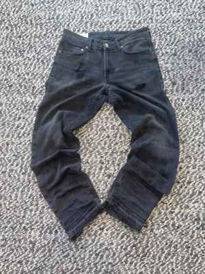 Svarta raka jeans - Säljer ett par svarta jeans med rak passform och klassisk femficksdesign. Jeansen har diskreta slitningar och är tillverkade i denim med en något stretchig känsla. Perfekta för en avslappnad och trendig look.