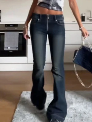 Mörkblå bootcut jeans med dragkedja - Säljer ett par mörkblå bootcut jeans med hög midja och en snygg, synlig dragkedja framtill. Jeansen har klassiska fem fickor och är tillverkade i stretchigt denimtyg som sitter tajt upptill och släpper ut vid benen. Perfekta för en trendig och avslappnad look.