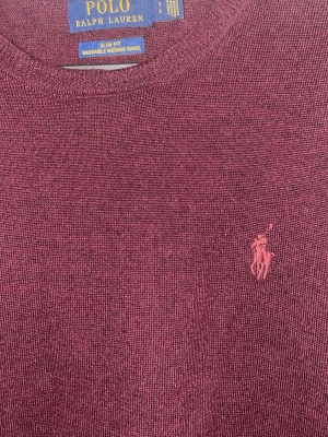 Vinröd merinoullströja Polo Ralph Lauren - Vinröd stickad tröja från Polo Ralph Lauren i slim fit-modell. Tillverkad i tvättbar merinoull och har rund halsringning samt det klassiska broderade logotypen på bröstet. Perfekt för dig som gillar stilrena och bekväma plagg.