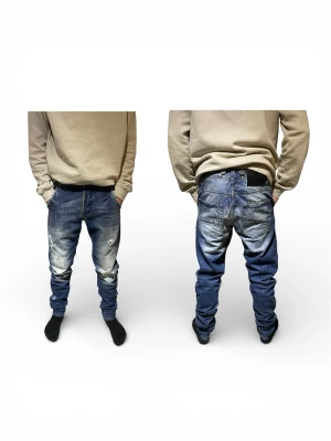 Adrian Hammond Jeans  - Säljer ett par blåa baggy jeans med tydliga slitningar och hål på framsidan från Adrian Hammond. Jeansen har en avslappnad passform, låg gren och klassiska fem fickor. Perfekta för en streetwear-look.