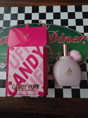 Candy Puff Eau de Parfum - Candy Puff Eau de Parfum från Omeeta kommer i en söt, rundad flaska med rosa detaljer och en fluffig rosa boll. Förpackningen är i stark rosa och vitt med guldtext. Doften är inspirerad av godis och passar dig som gillar söta parfymer.