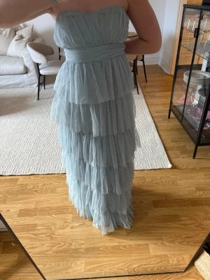 Ljusblå axelbandslös långklänning - Säljer en ljusblå axelbandslös långklänning från BEAUUT med flera lager volanger och markerad midja. Klänningen har en romantisk look och är perfekt för speciella tillfällen. Materialet känns lätt och luftigt.