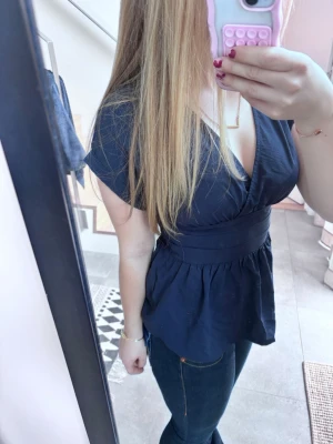 Mörkblå topp med v-ringning - Säljer en mörkblå top med v-ringad hals. Perfekt att styla med jeans eller kjol för en trendig look. Helt oanvänd!