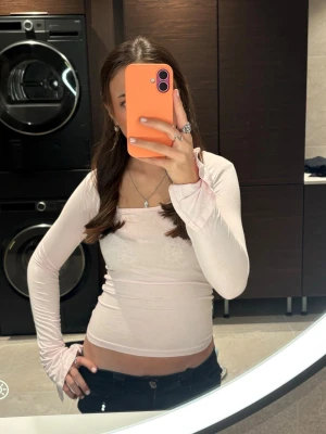 Ljusrosa långärmad croppad topp - Trendig ljusrosa långärmad topp med croppad passform och fyrkantig halsringning. Perfekt för att skapa en snygg och modern look. Materialet känns mjukt och stretchigt, vilket gör den bekväm att bära. Passar utmärkt till jeans eller kjol.