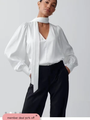 SÖKER!!!!Vit blus med scarf från Gina  tricot - Stilren vit blus från Gina tricot  med v-ringning och långärmade puffärmar. Blusen har en elegant scarf-detalj runt halsen och breda manschetter. Materialet är lätt och ger ett lyxigt intryck.