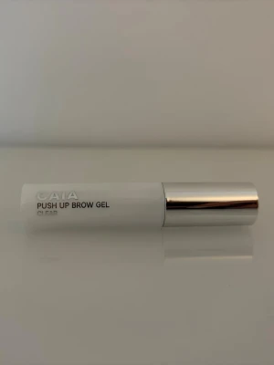 Ny! CAIA Push Up Brow Gel Clear - Ny! Transparent ögonbrynsgel från CAIA i en stilren vit tub med silverfärgat lock. Perfekt för att forma och fixera brynen utan färg. Enkel att applicera med borste och ger ett naturligt resultat. Snygg och modern design som passar i sminkväskan.