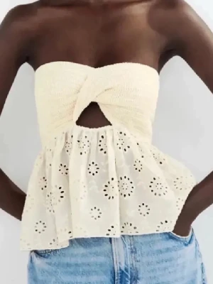 Krämvit axelbandslös spets-tubtopp - Söt krämvit tubtopp med twistad byst och broderad spetsdetalj nedtill. Toppen är axelbandslös och har ett litet hål framtill. Perfekt till jeans eller kjol för en fräsch sommarlook.