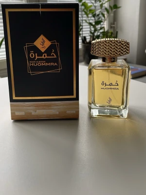 HUOMMRA parfym med guldig kork - Exklusiv parfym från Wash Alrayah, HUOMMRA, i en stilren fyrkantig glasflaska med guldig vätska och en snyggt mönstrad guldig kork. Kommer i elegant svart och guldig förpackning. Perfekt för dig som gillar lyxiga dofter.