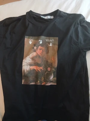 Svart Off-White t-shirt med caravaggio boy tryck - Svart t-shirt från Off-White med ett stort caravaggio tryck på framsidan och vit text på ryggen. Baggy passform och rund hals. Perfekt för dig som gillar streetwear.