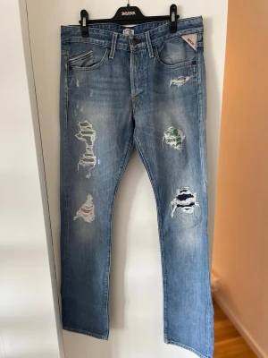Ljusblå slitna jeans från Replay - Säljer ett par skitsnygga ljusblå jeans från Replay med flera unika slitningar! Jeansen är i storlek W32 L34 och har as snygga tygbitar insydda i slitningarna. Jeansen är i väldigt bra kvalite och väl omhändertagna!