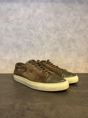 Axel Arigato Clean 90 - Säljer dessa Axel Arigato Clean 90s i Snygg brun mocka med vit sula och mörkgrå gummitå. Klassisk siluett med snörning och diskret design som passar till det mesta. Materialmixen ger en cool kontrast och en modern känsla. I bra skick utöver slitage på tån ( vanligt slitage från användning) inget som påverkar funktionen!