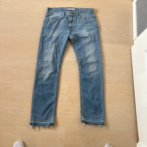 Levi's 504 straight  - Ljusblå raka jeans från Levi's med klassisk femficksdesign och slitna, fransiga benslut. Jeansen har en avslappnad passform och tydliga slitningar framtill för en vintagekänsla. Perfekta för en casual och trendig look.