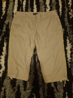 Beige shorts med snörning - Säljer ett par beige shorts med snörning i bensluten och knappgylf. De har normal passform, sidofickor fram och fickor bak. Perfekta för varma dagar och enkel stil.