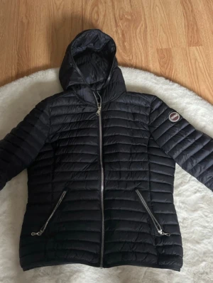 jacka från Colmar i nyskick - Snygg marinblå pufferjacka från Colmar med huva och två dragkedjeförsedda fickor framtill. Jackan har ett quiltat mönster och Colmar-logga på ärmen. Perfekt för kalla dagar och riktigt stilren look.